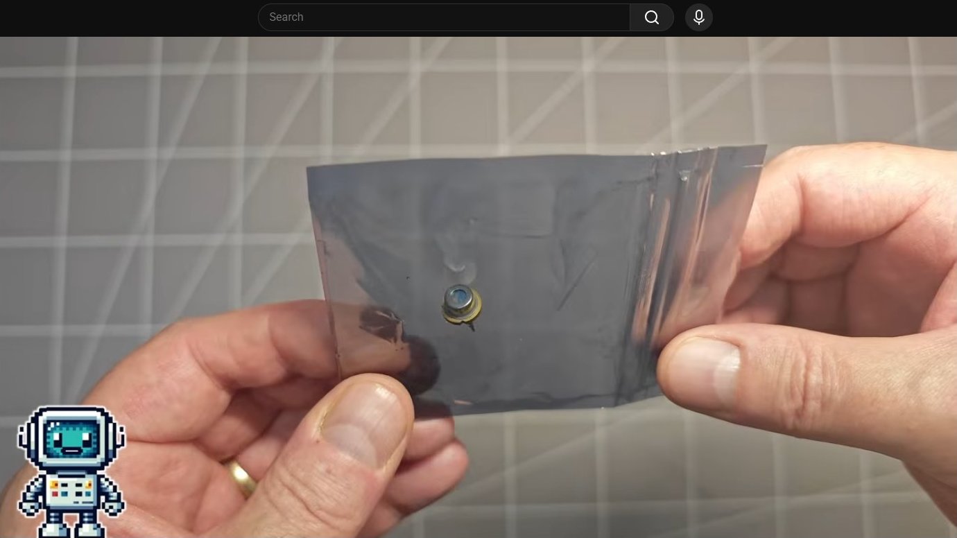 Laser diode component held between fingers against gray backdrop