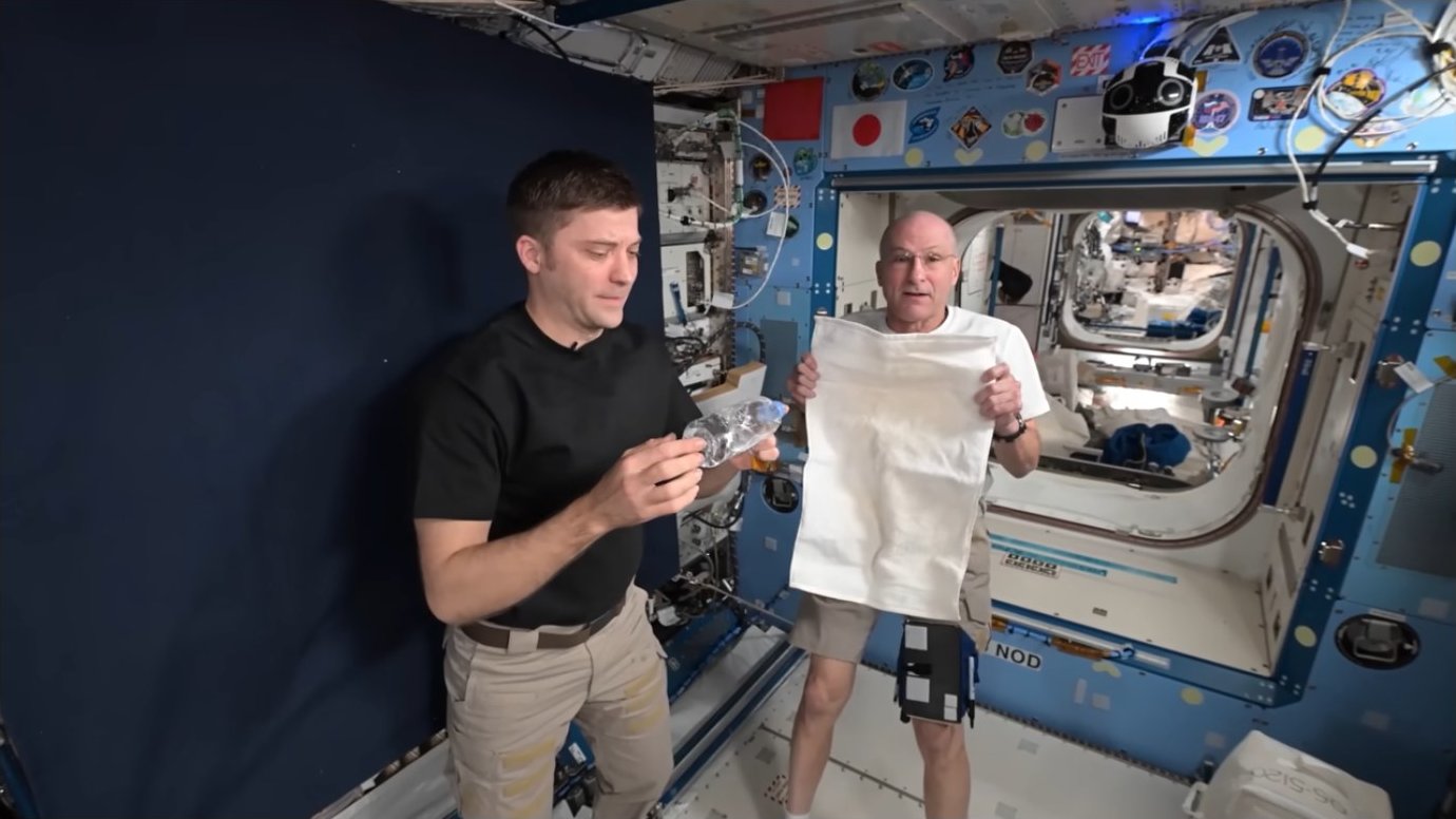 Two astronauts demonstrating with water bottles and a towel in microgravity