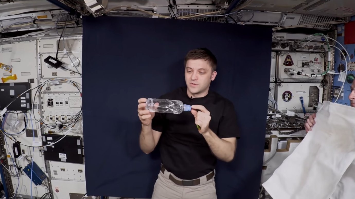 Astronaut examining a water bottle filled with liquid and bubbles