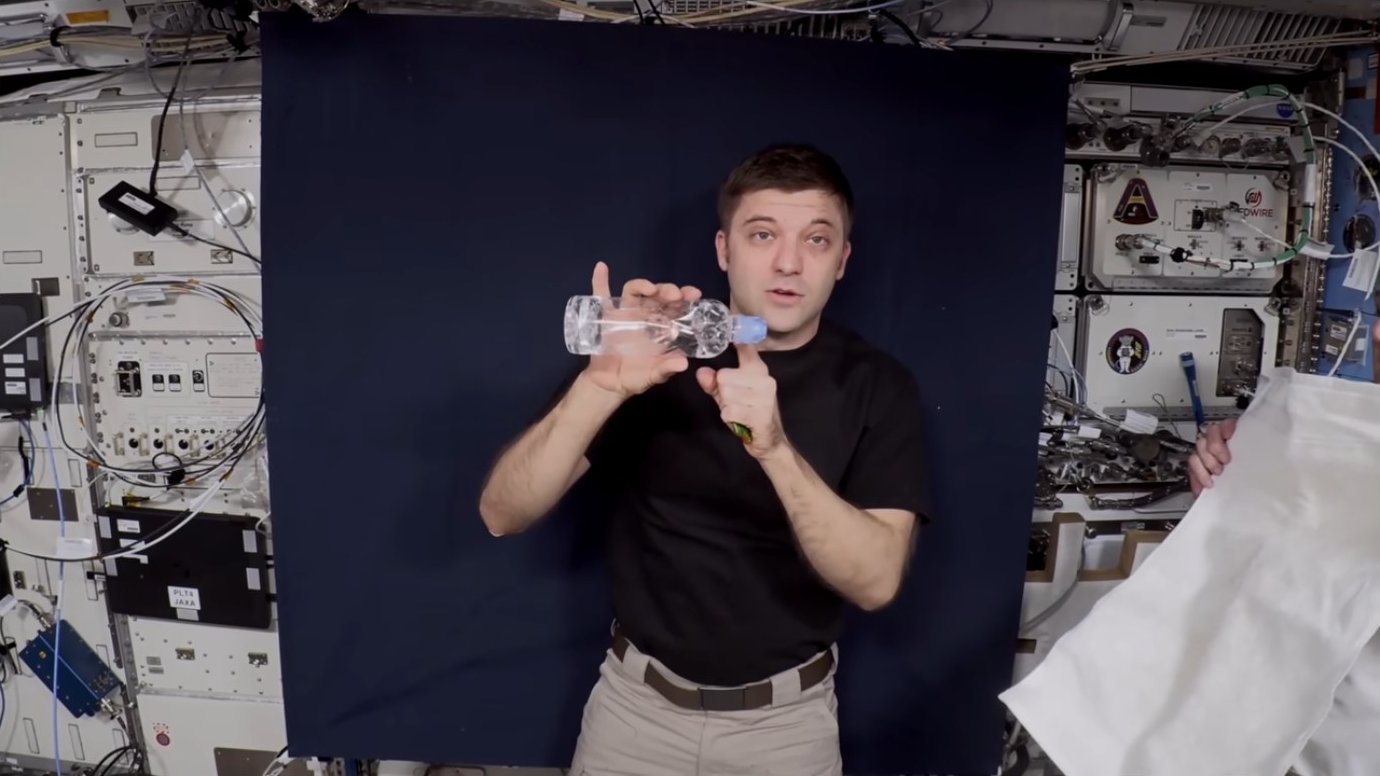 Astronaut demonstrating rotation concept with a water bottle
