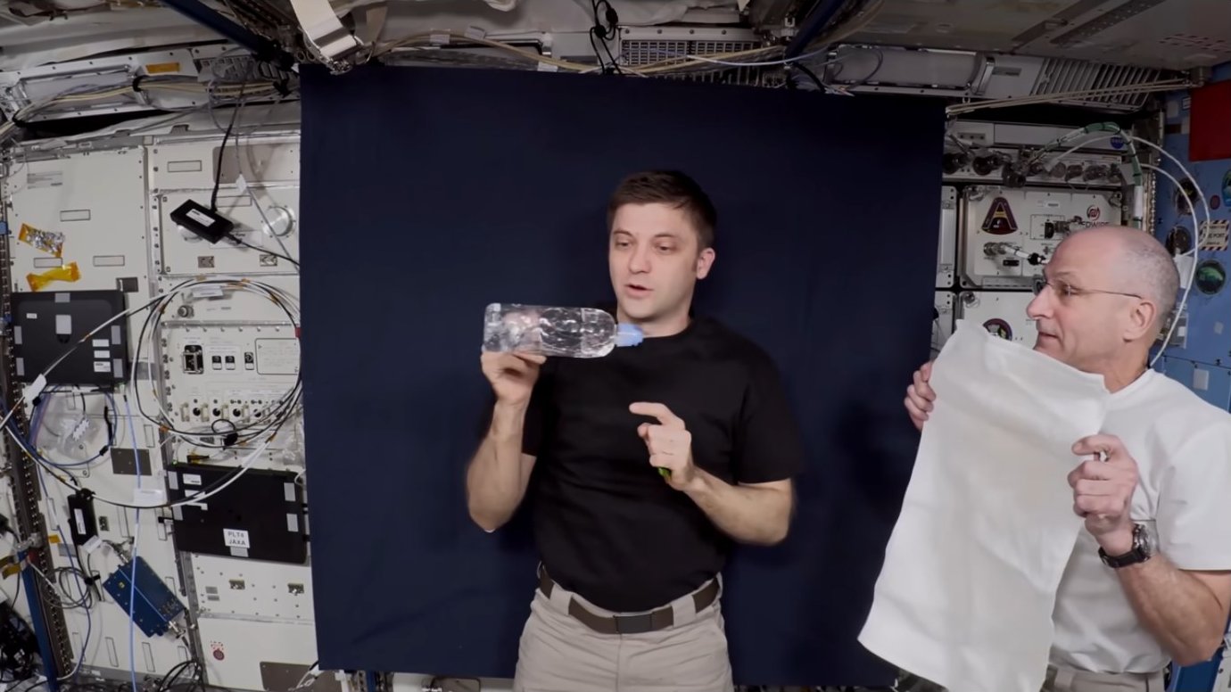 Two astronauts with connected water bottles and a towel in preparation