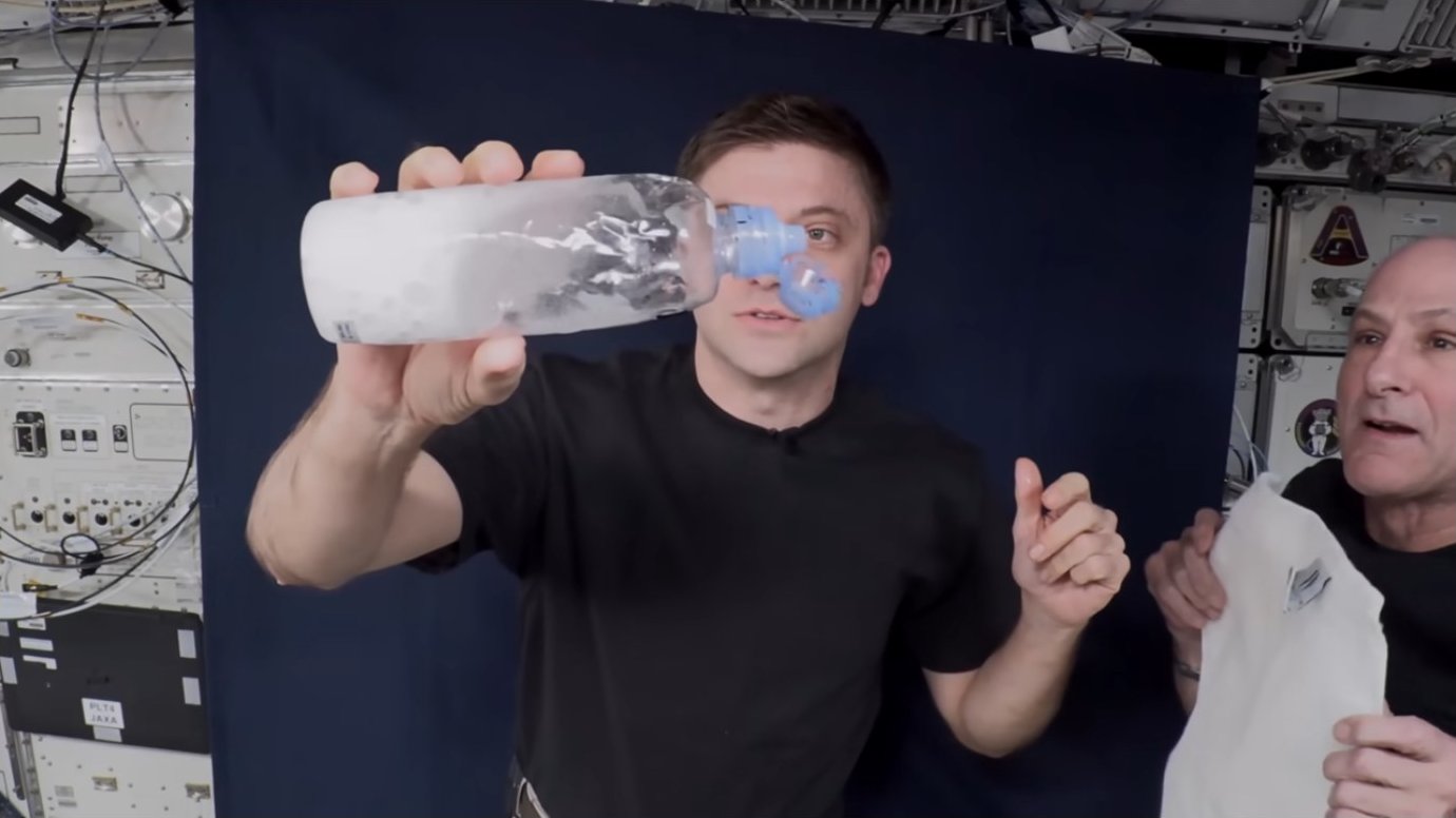 Astronaut holding combined water bottles up to the camera