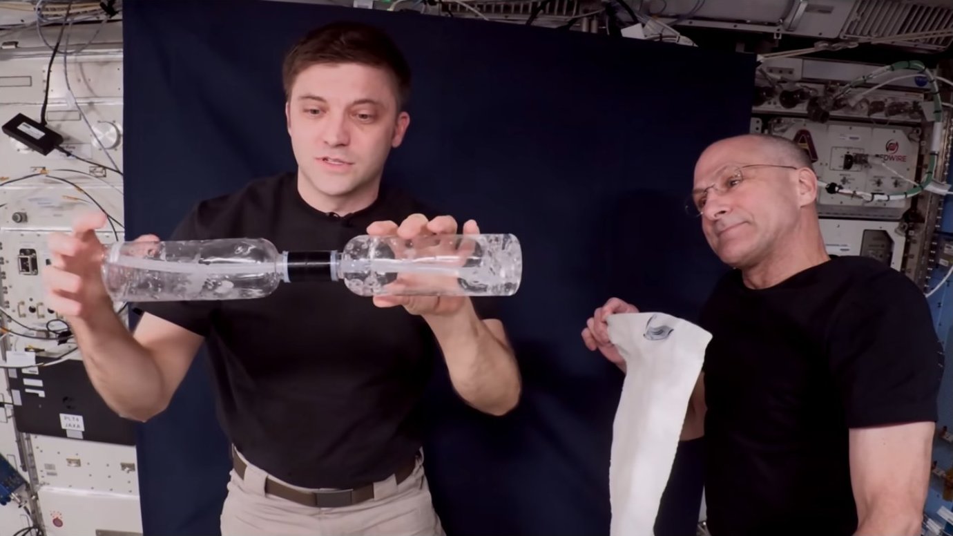 Astronauts holding connected transparent bottles with liquid and connecting tube