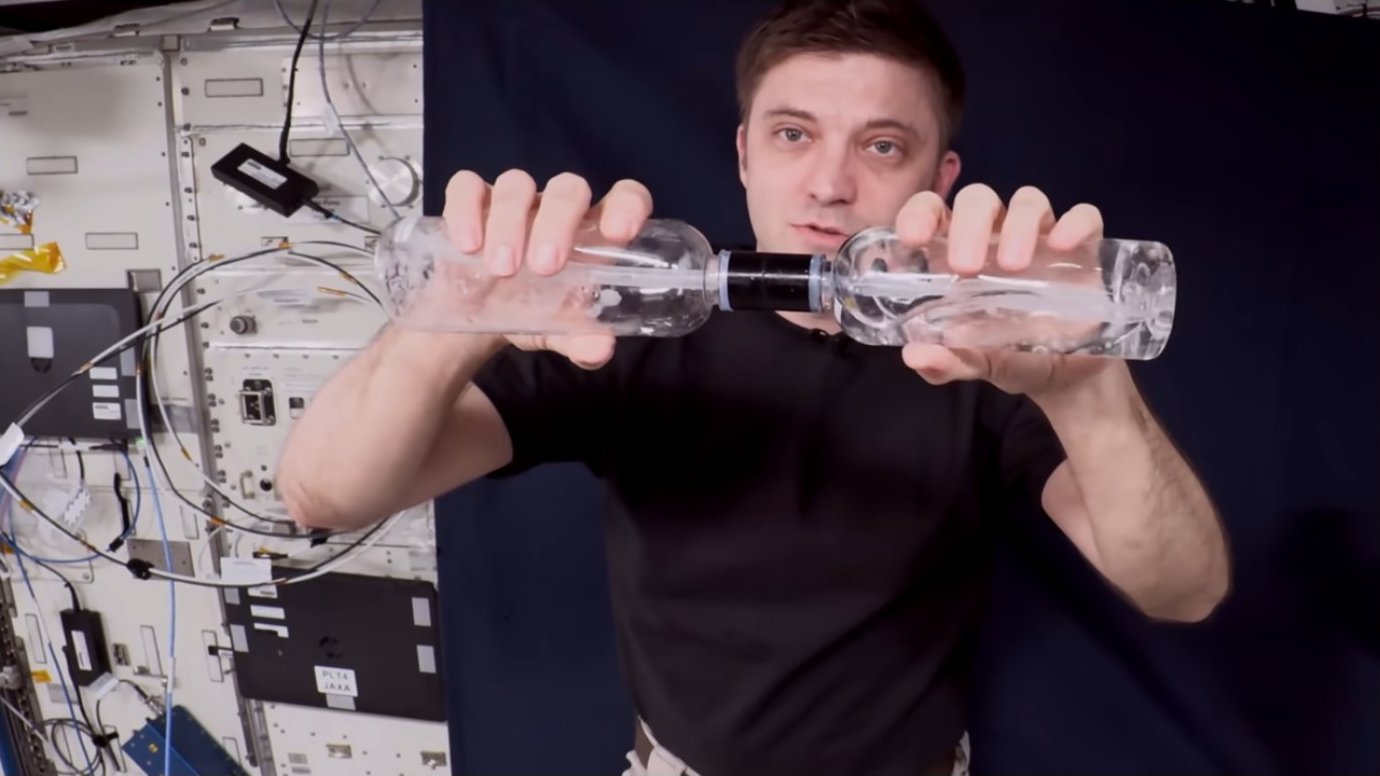 Close-up of astronaut holding connected water bottles showing fluid and gas separation
