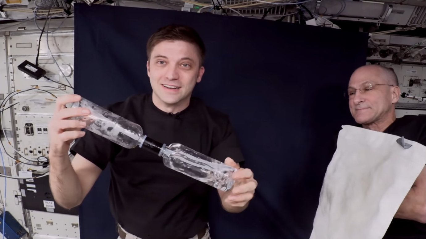 Astronauts displaying the connected bottle system with visible liquid transfer
