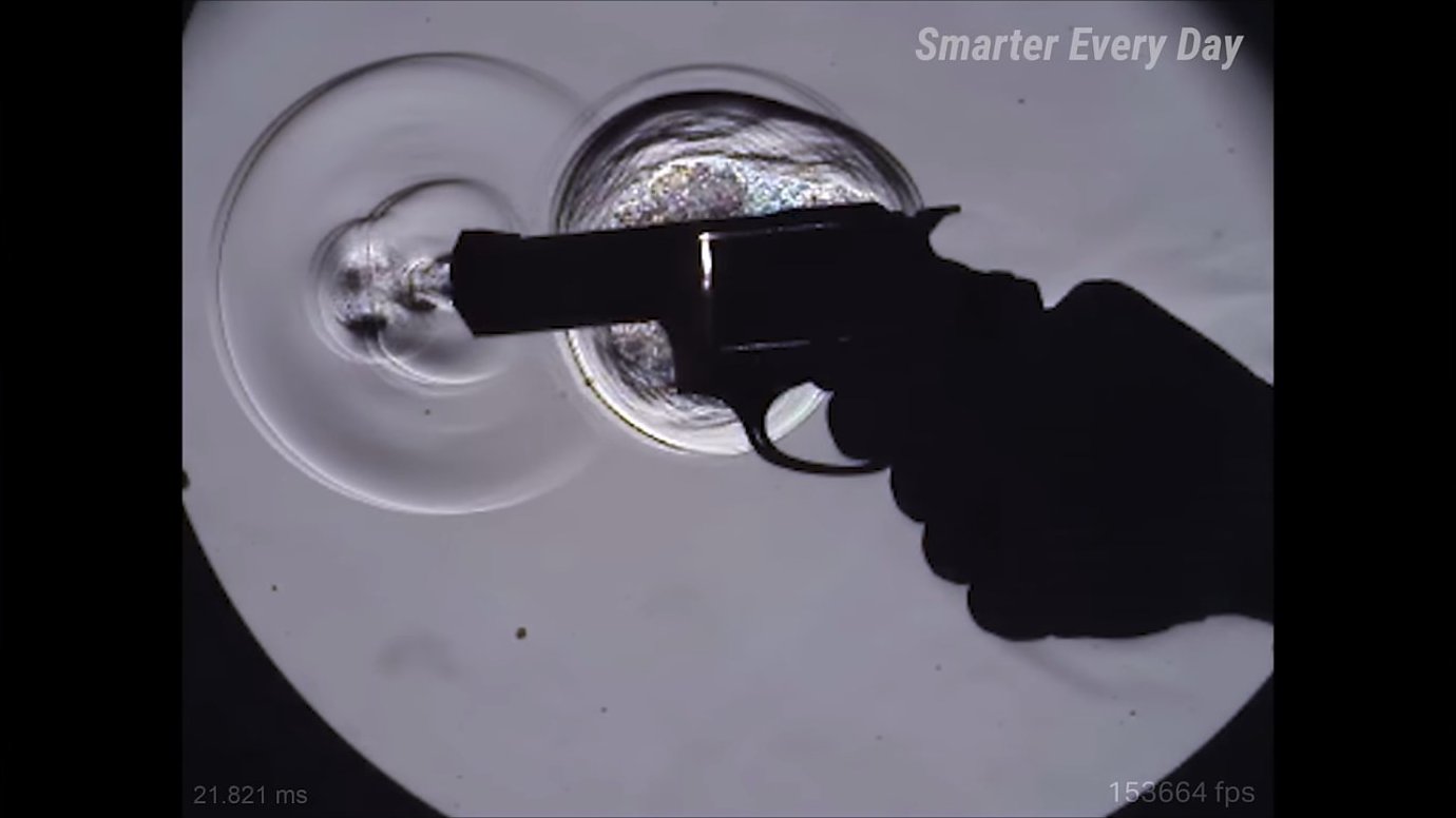 A revolver firing, captured in extreme slow motion. Jets of gas and visible shock waves leak from the cylinder gap perpendicular to the barrel, illustrating why hand placement near the cylinder is dangerous.