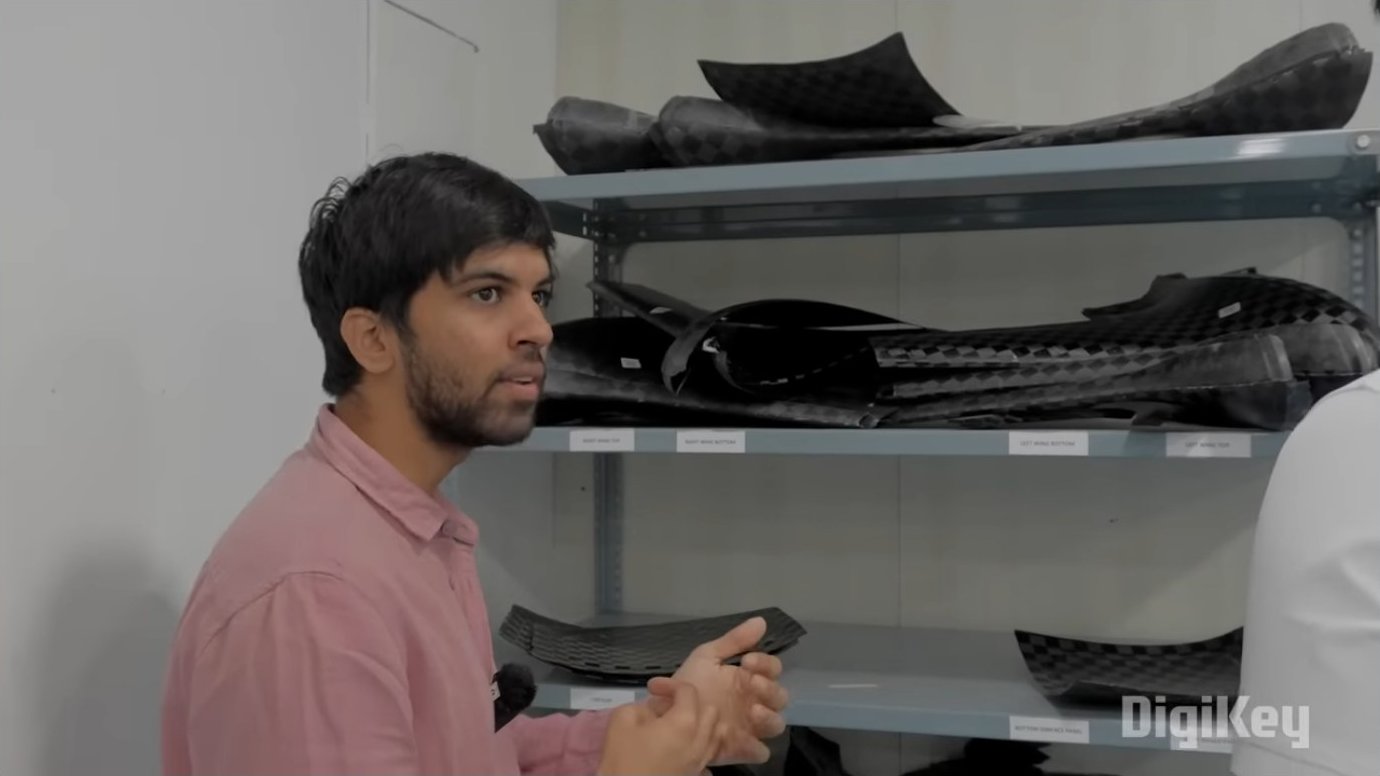 Shelves holding various carbon fiber and aramid composite parts for drone assembly. Each airframe requires eighteen separate composite components, from wing halves to motor mounts, all produced in-house using vacuum-bagging and autoclave curing processes.