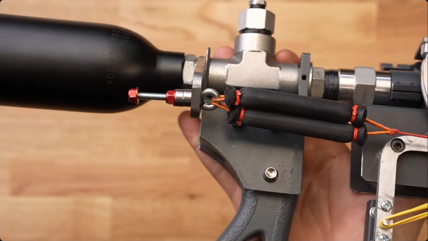 Close-up of the modified ball valve assembly showing custom-machined trigger components and attachment points for the elastic actuator system that will snap the valve open against internal pressure.